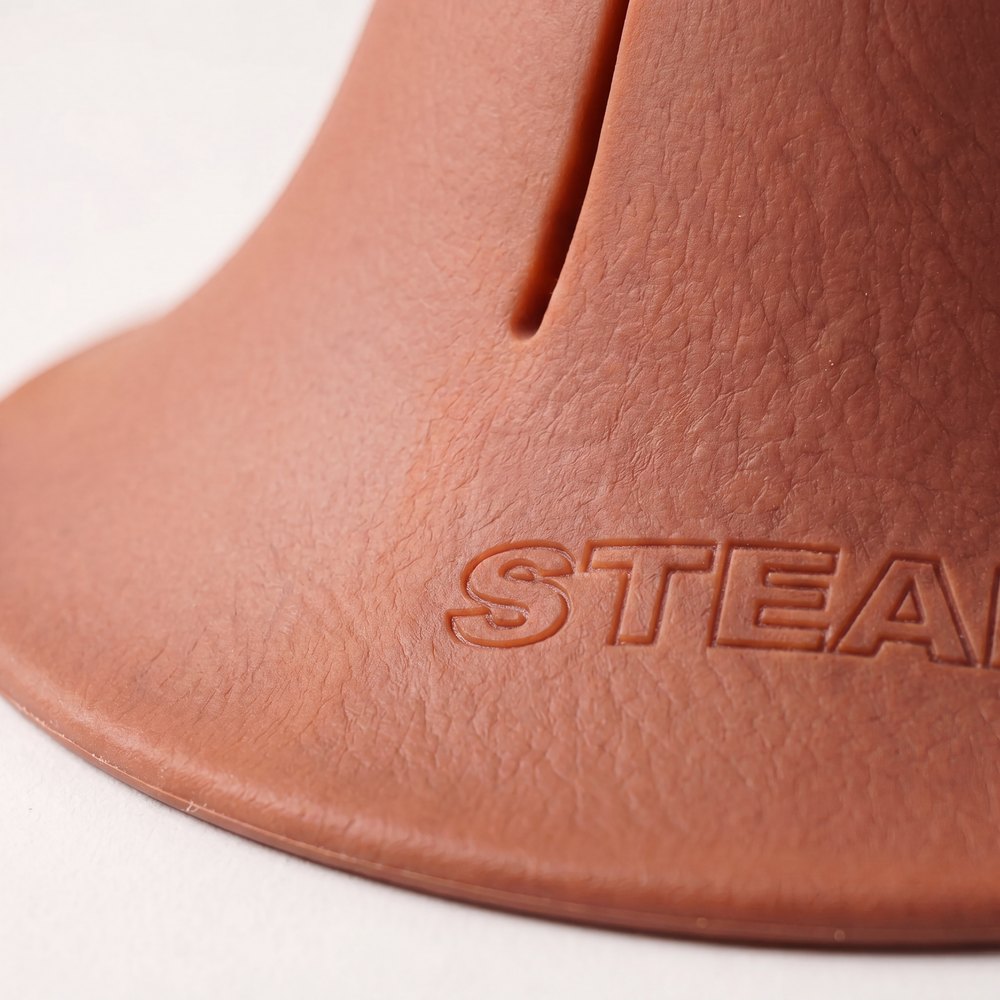 A macro photograph of the flared foot of a terracotta Steadi, showing the moulded STEADI mark and the grain of the material.